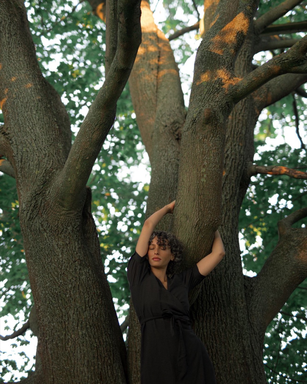 Jennifer Tara mit geschlossenen Augen an einem großen Baum, in organische Formen geschnitten